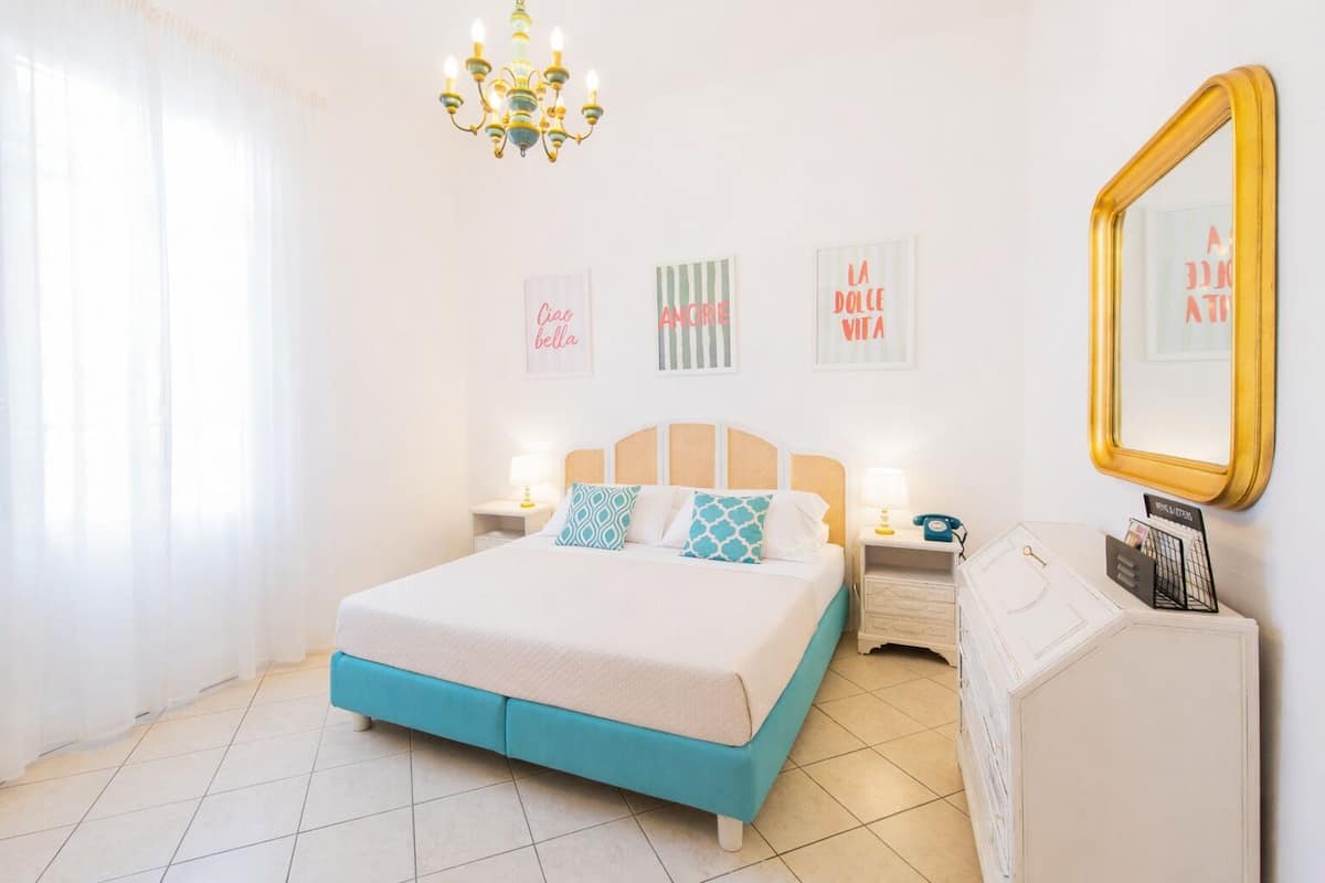 Une chambre à coucher comprenant un lit, des tables de chevet, une commode, un meuble à tiroirs, un miroir et des œuvres d’art murales.