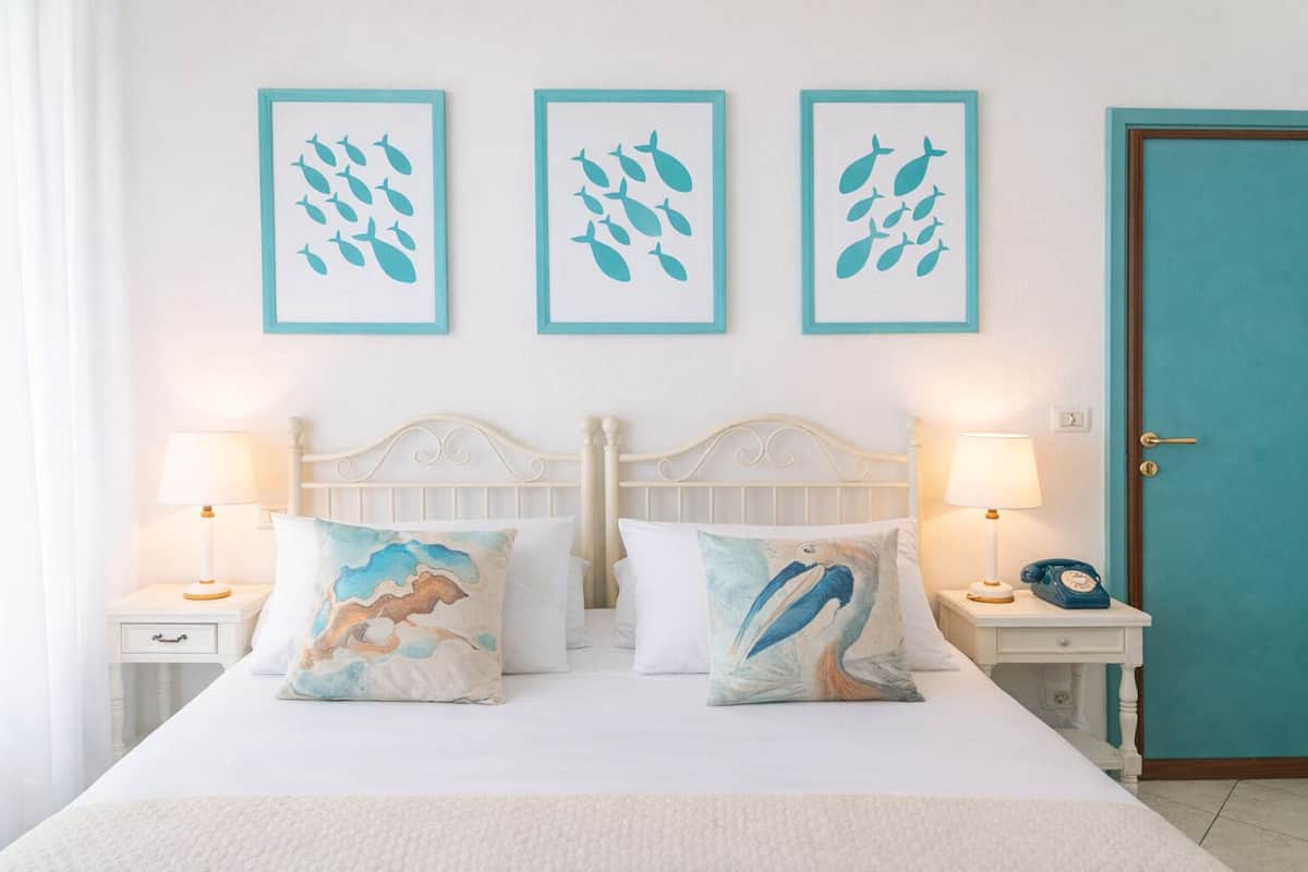 Un lit avec deux oreillers blancs, deux tables de chevet avec des lampes et trois œuvres d’art encadrées accrochées au mur au-dessus du lit.