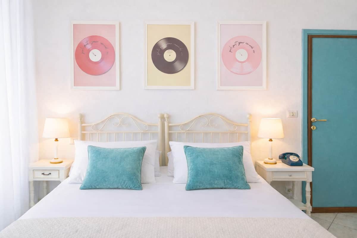 Un lit avec une literie blanche et des coussins turquoise, flanqué de tables de chevet avec des lampes, et trois pochettes de disques vinyles encadrées accrochées au mur.