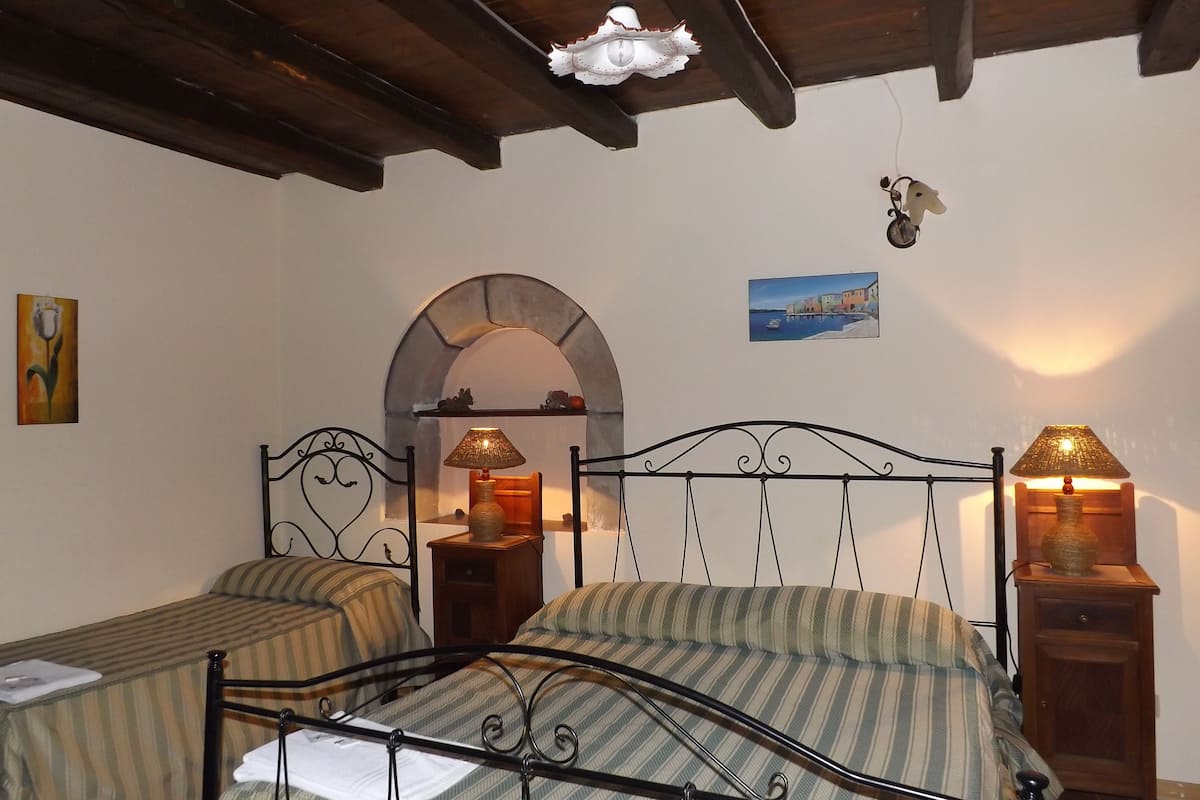 A bedroom with two single beds, a wooden ceiling, a stone archway, and a painting on the wall.