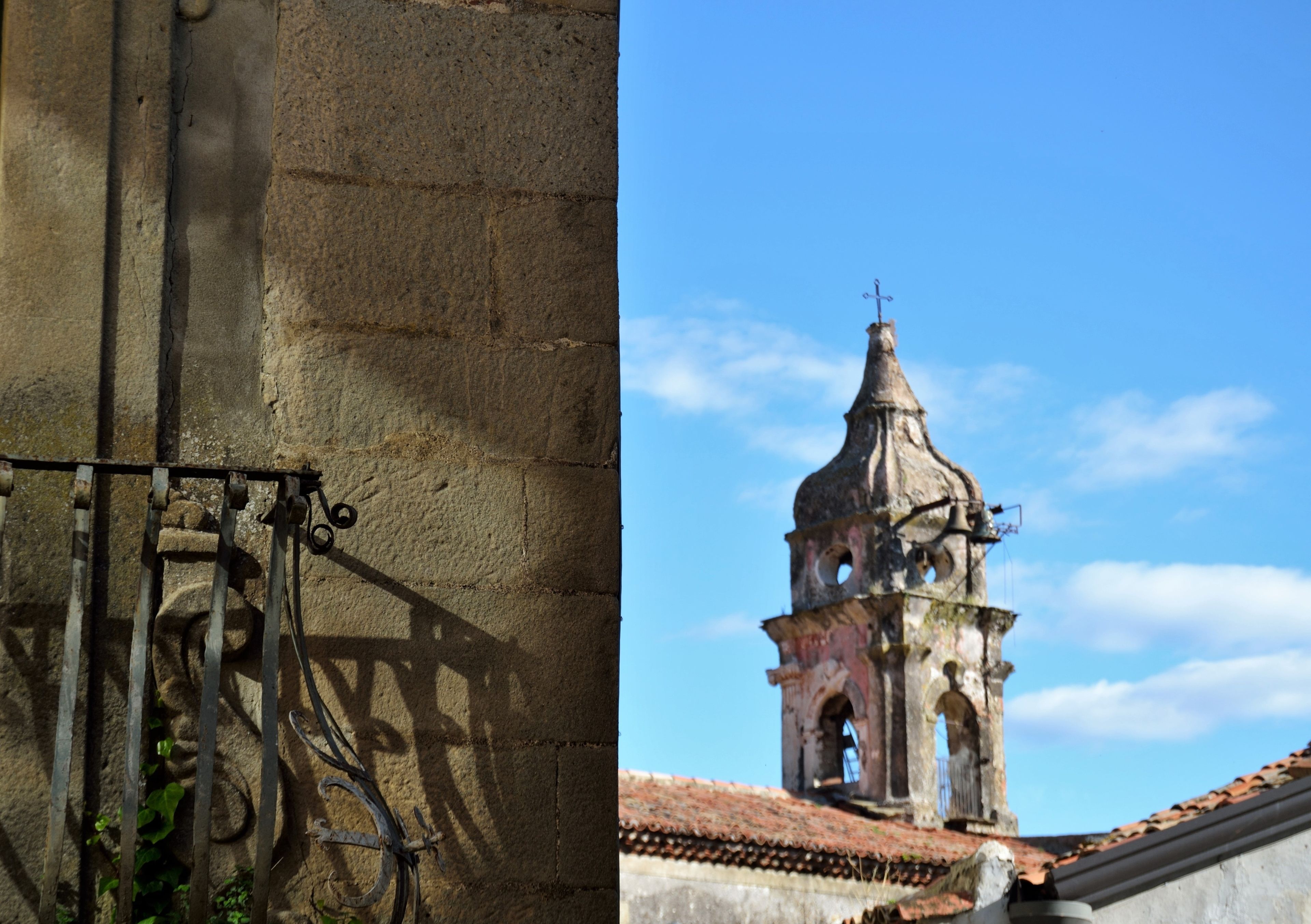 A stone wall with a metal gate and a bell tower in the background.