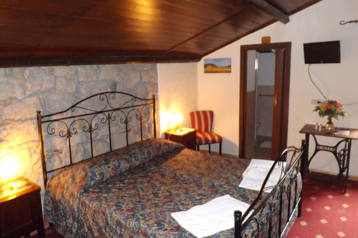 A bedroom with a bed, a chair, a desk, a mirror, and a stone wall.