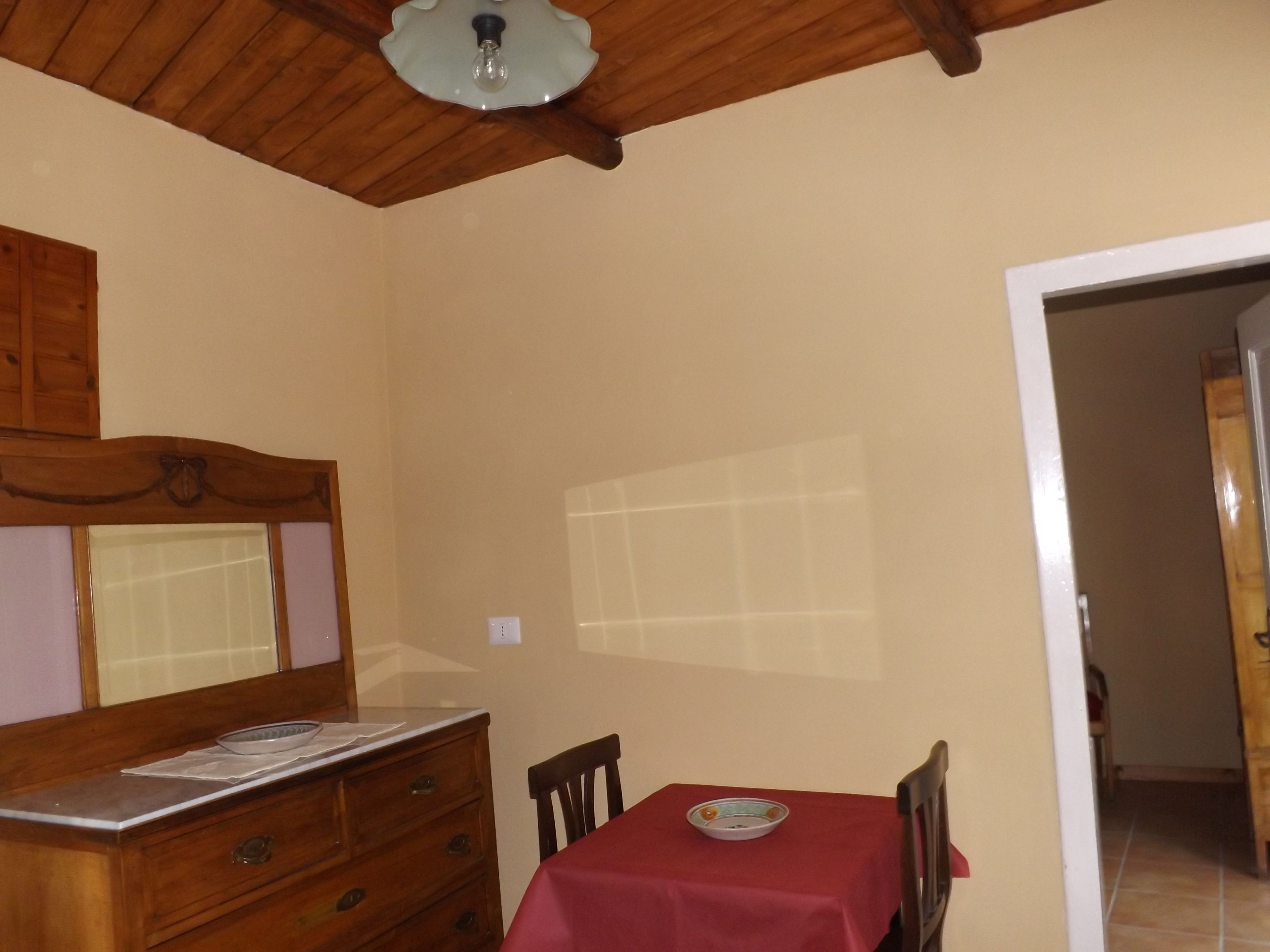 A room with a wooden dresser, a table with a red tablecloth, and a ceiling light fixture.