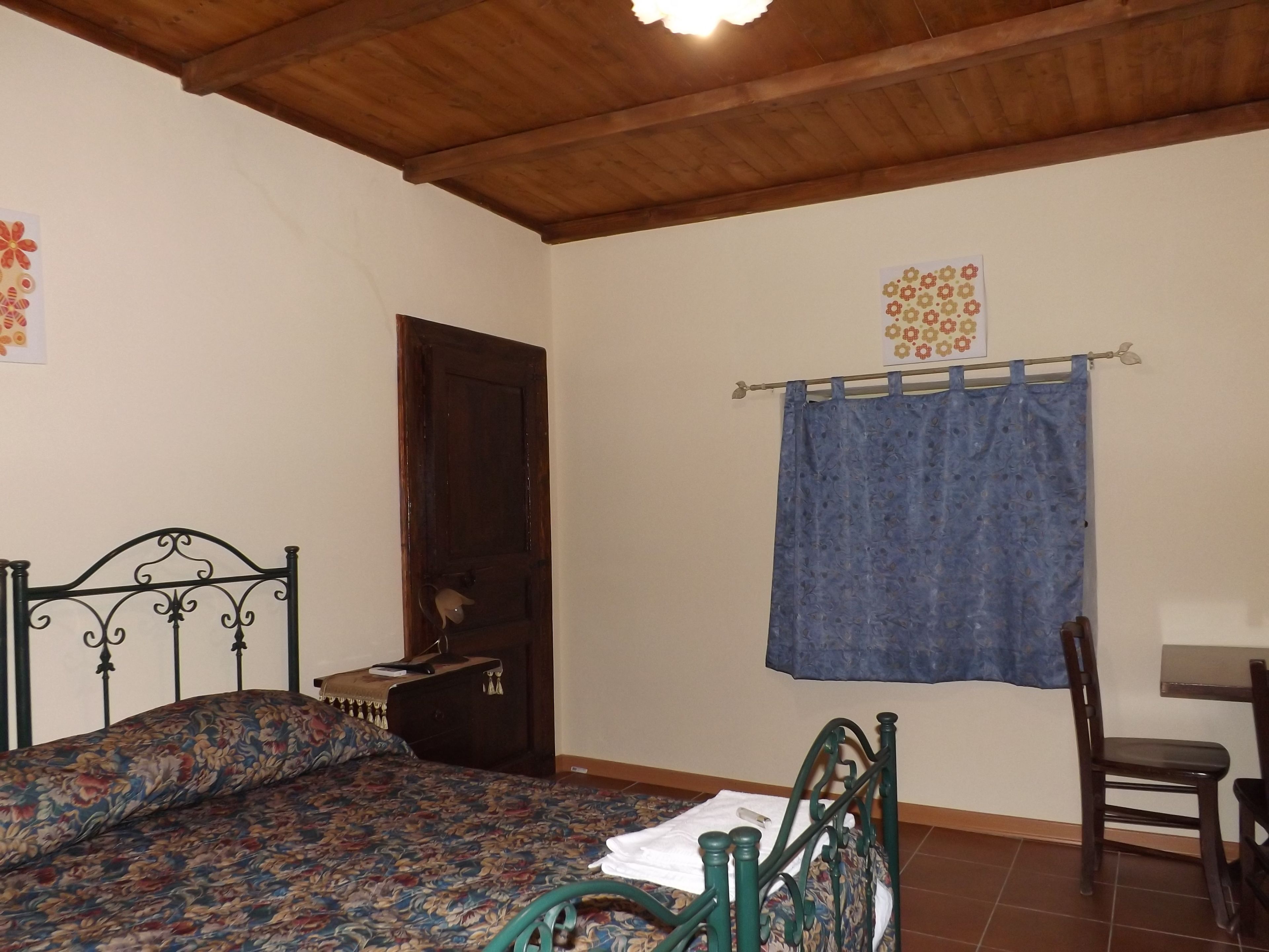 A bedroom with a bed, a chair, a wooden door, and a curtain.