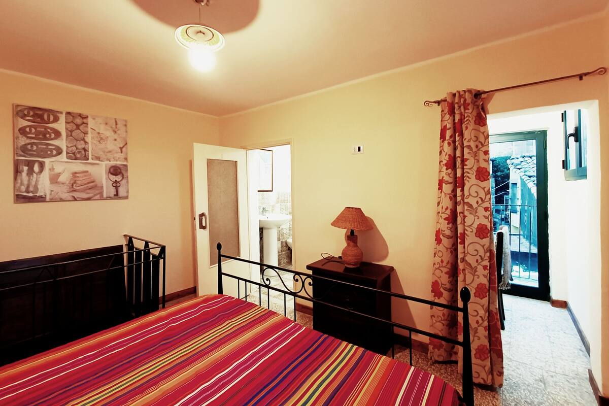A bedroom with a bed, a nightstand, a lamp, and a door leading to a balcony.