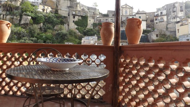 Un balcón con una mesa redonda de metal, dos macetas de cerámica y una verja decorativa de metal.