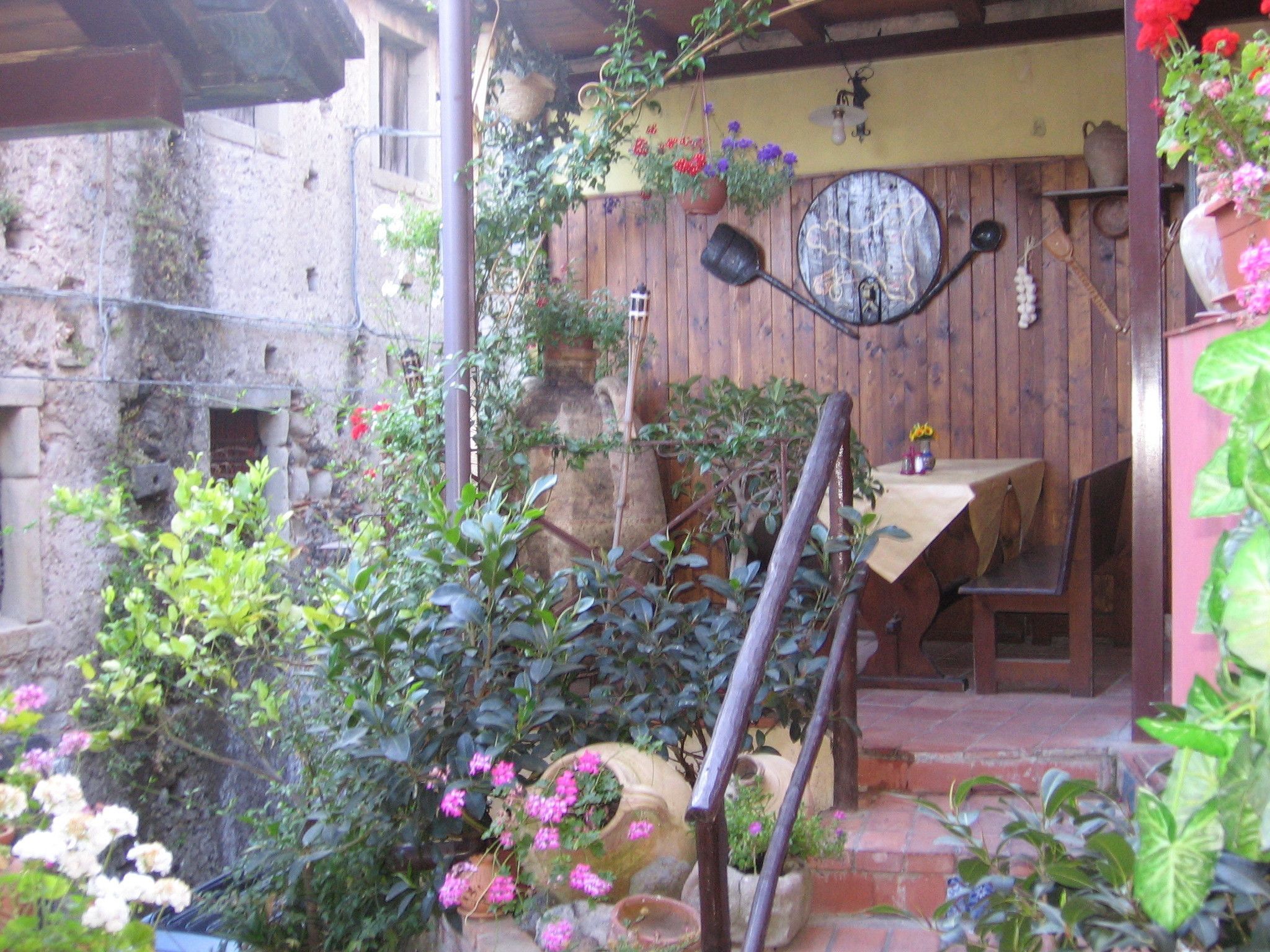 A rustic outdoor area with a wooden table and chairs, surrounded by potted plants and flowers.
