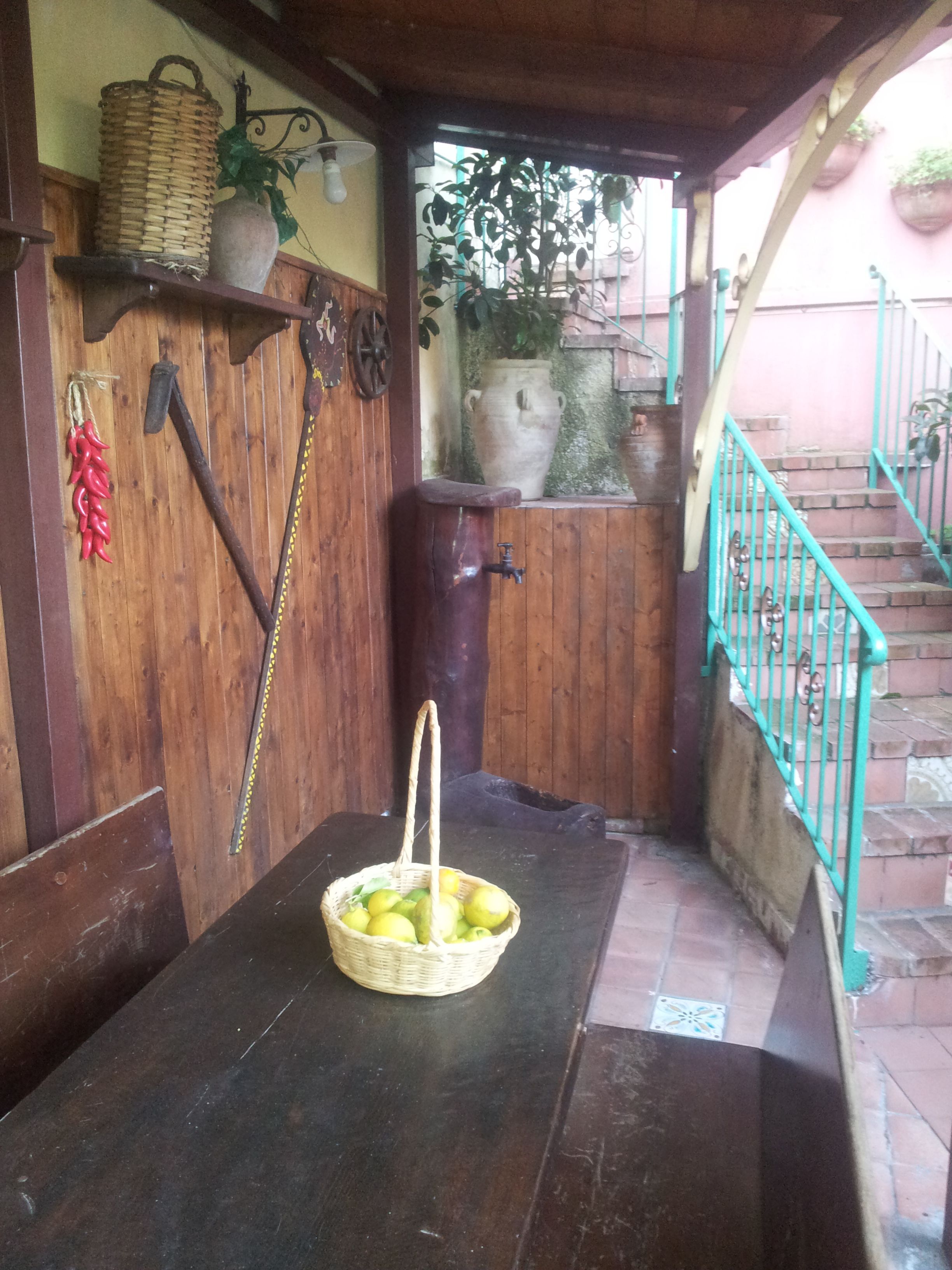 A wooden table with a basket of lemons, a hanging light fixture, and a rustic wall with a potted plant.