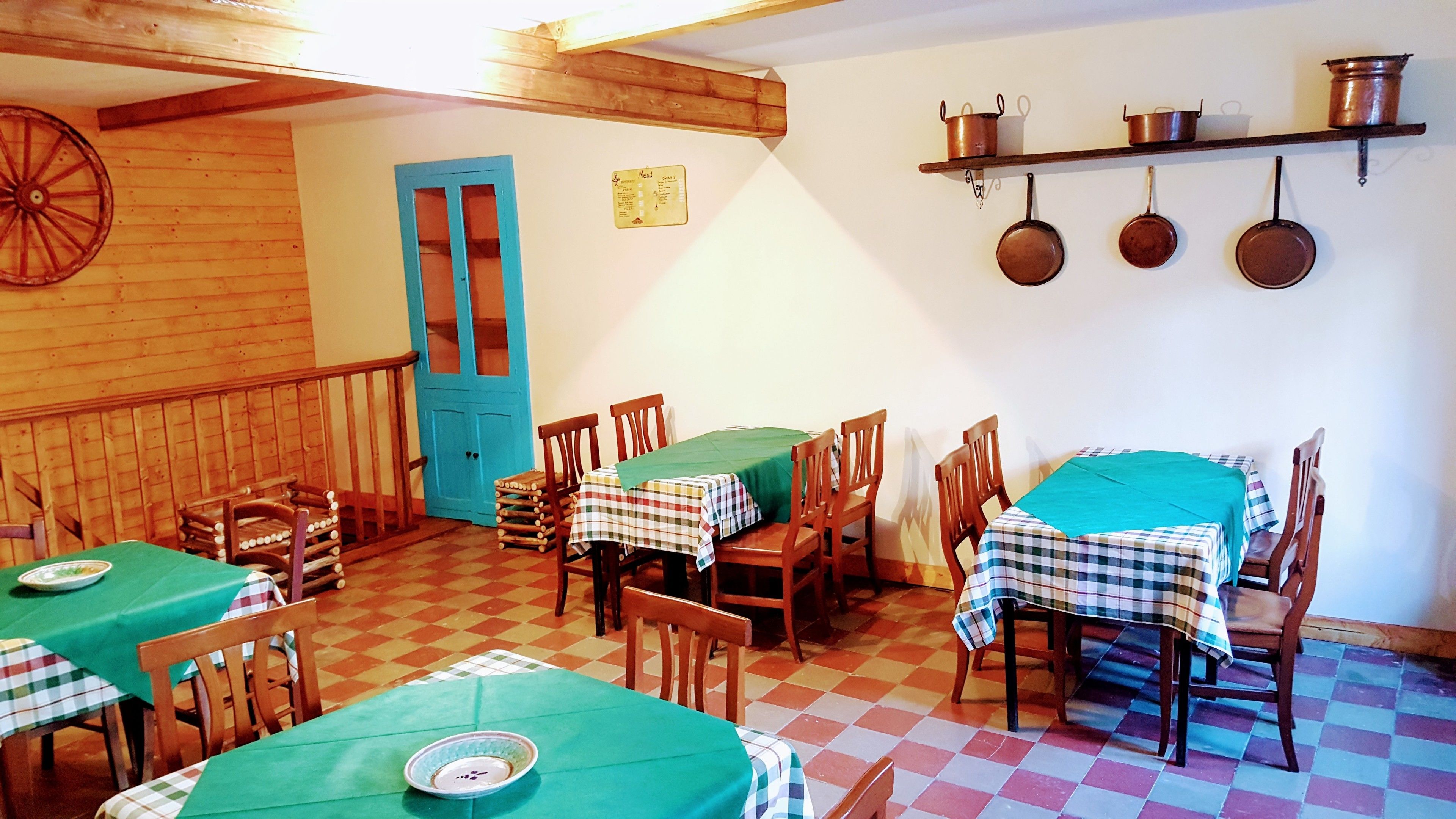 A dining area with wooden tables and chairs, a blue door, and copper pots hanging on the wall.