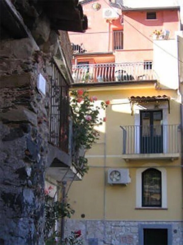 A building with a stone facade, a balcony with a metal railing, and a window with an air conditioning unit. - Albergo Diffuso Borgo Santa Caterina "Quartiere Ebraico" (Castiglione di Sicilia)