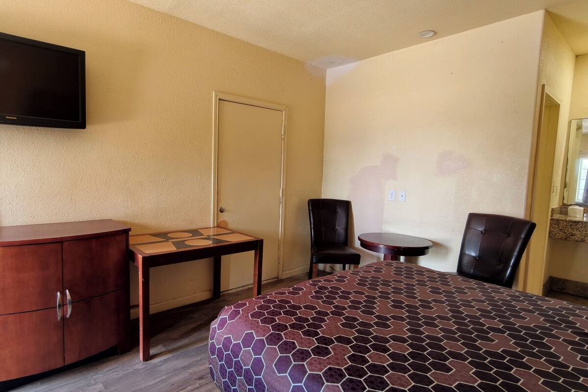 A hotel room with a bed, a desk, a chair, a television, and a door.