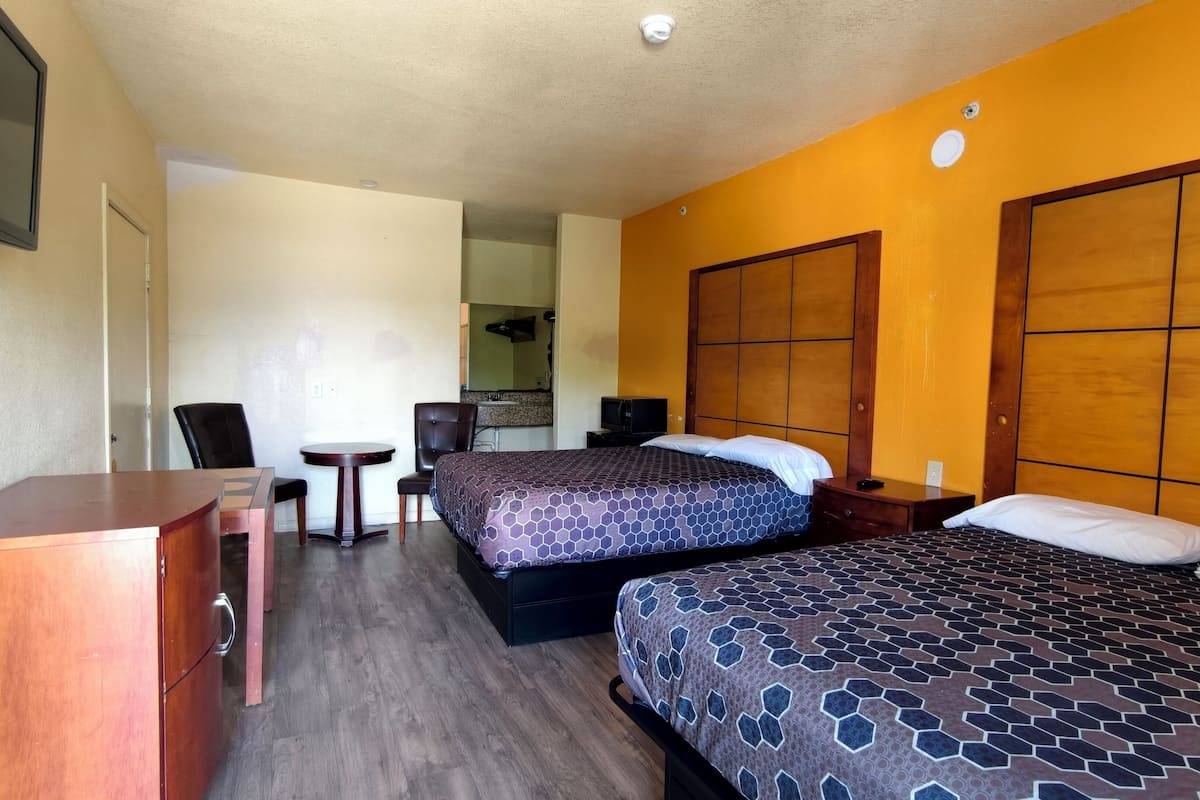 A hotel room with two beds, a desk, a chair, a television, and a bathroom visible in the background.
