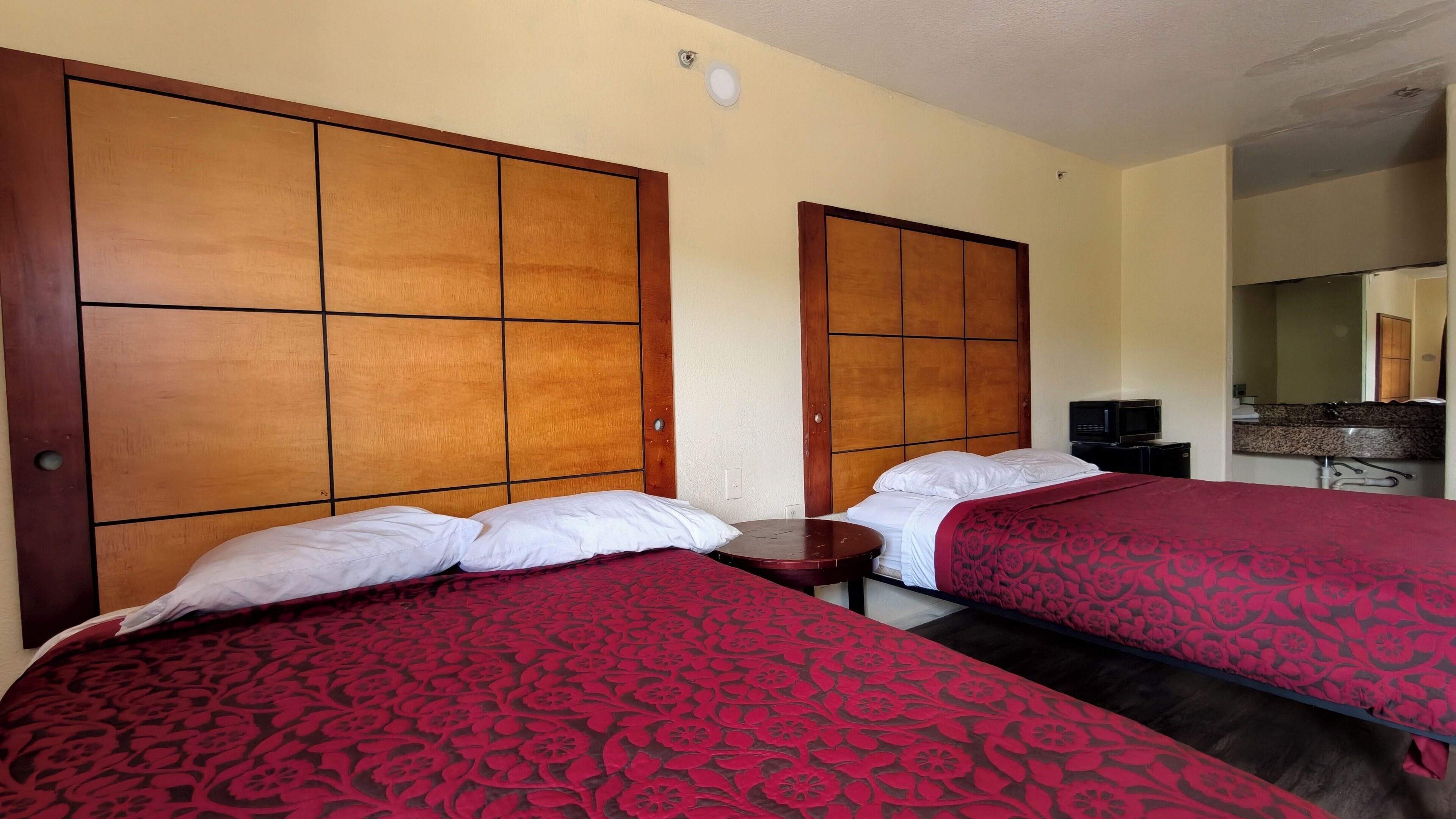 Une chambre d’hôtel avec deux lits, une tête de lit en bois, une petite table, un téléviseur et une salle de bain visible au fond.