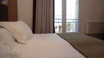 Habitación de hotel con cama, balcón con una silla y vistas a la ciudad.