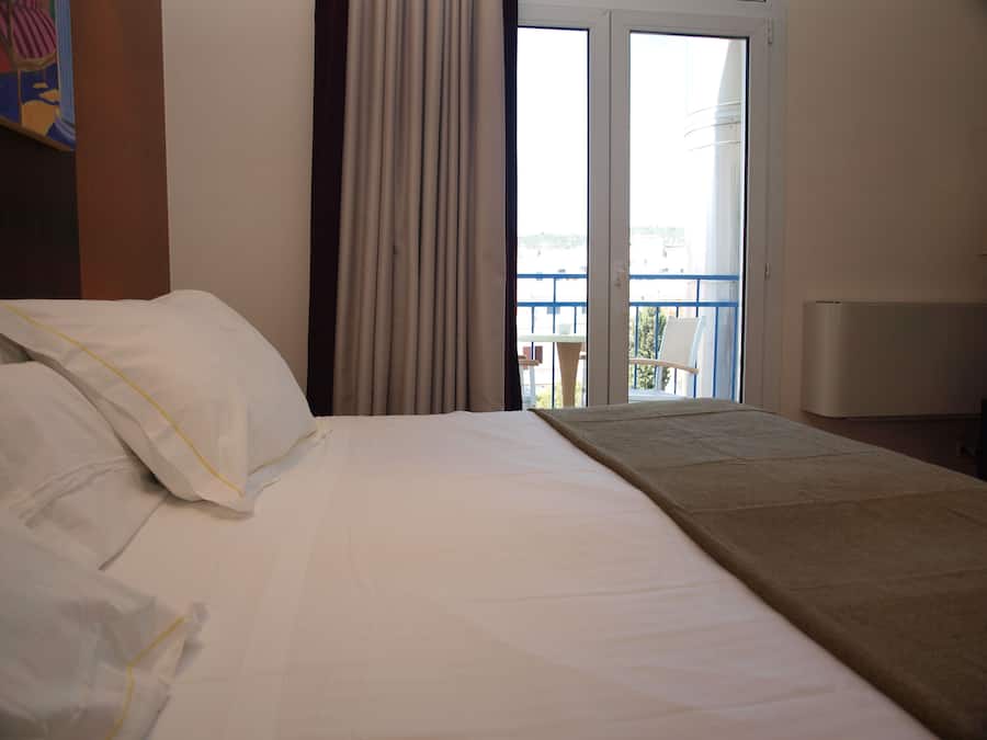Habitación de hotel con cama, balcón con una silla y vistas a la ciudad.