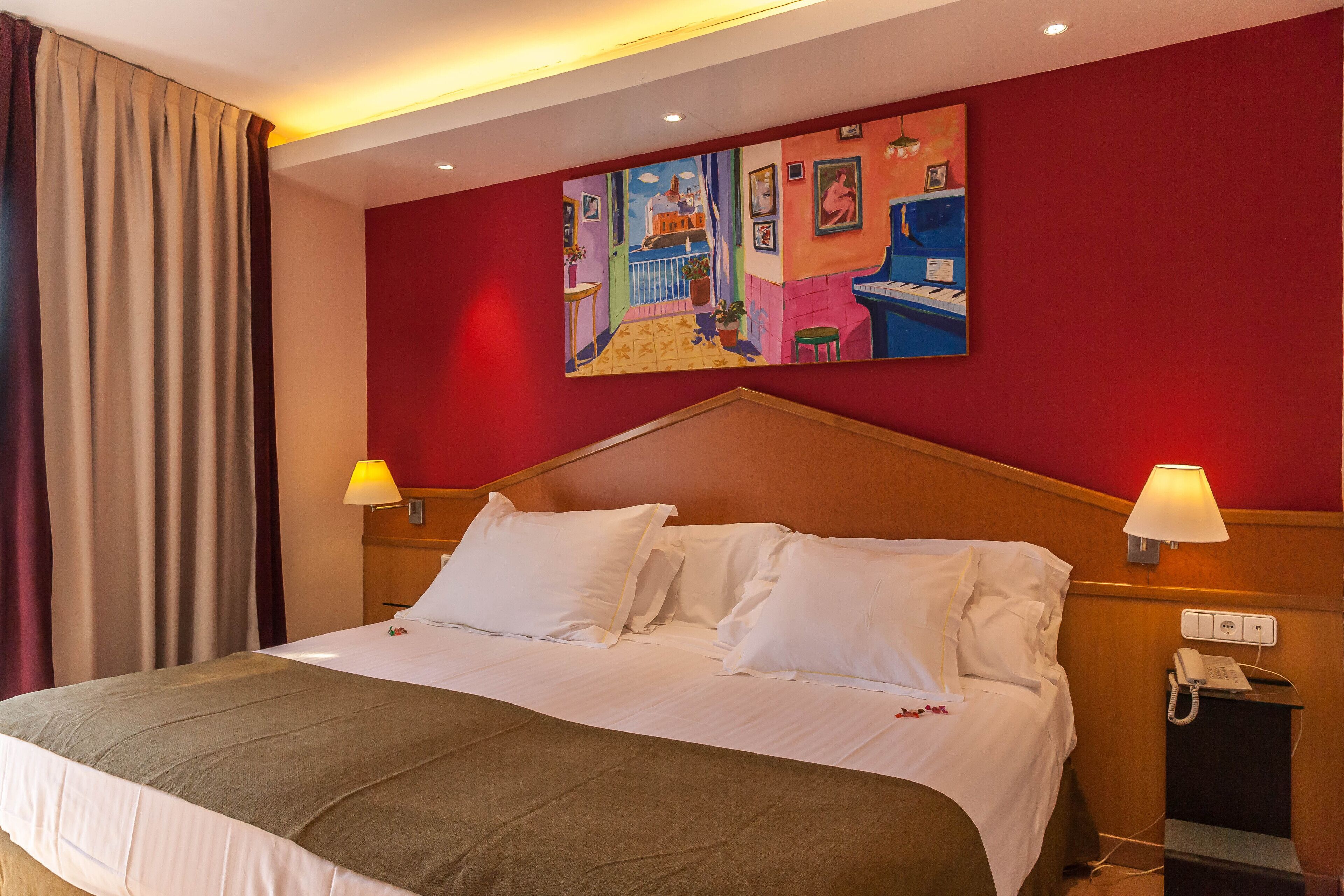 A hotel room with a large bed, two bedside lamps, a painting on the wall, and a telephone on the nightstand.