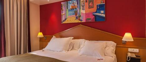 A hotel room with a large bed, two bedside lamps, a painting on the wall, and a telephone on the nightstand.