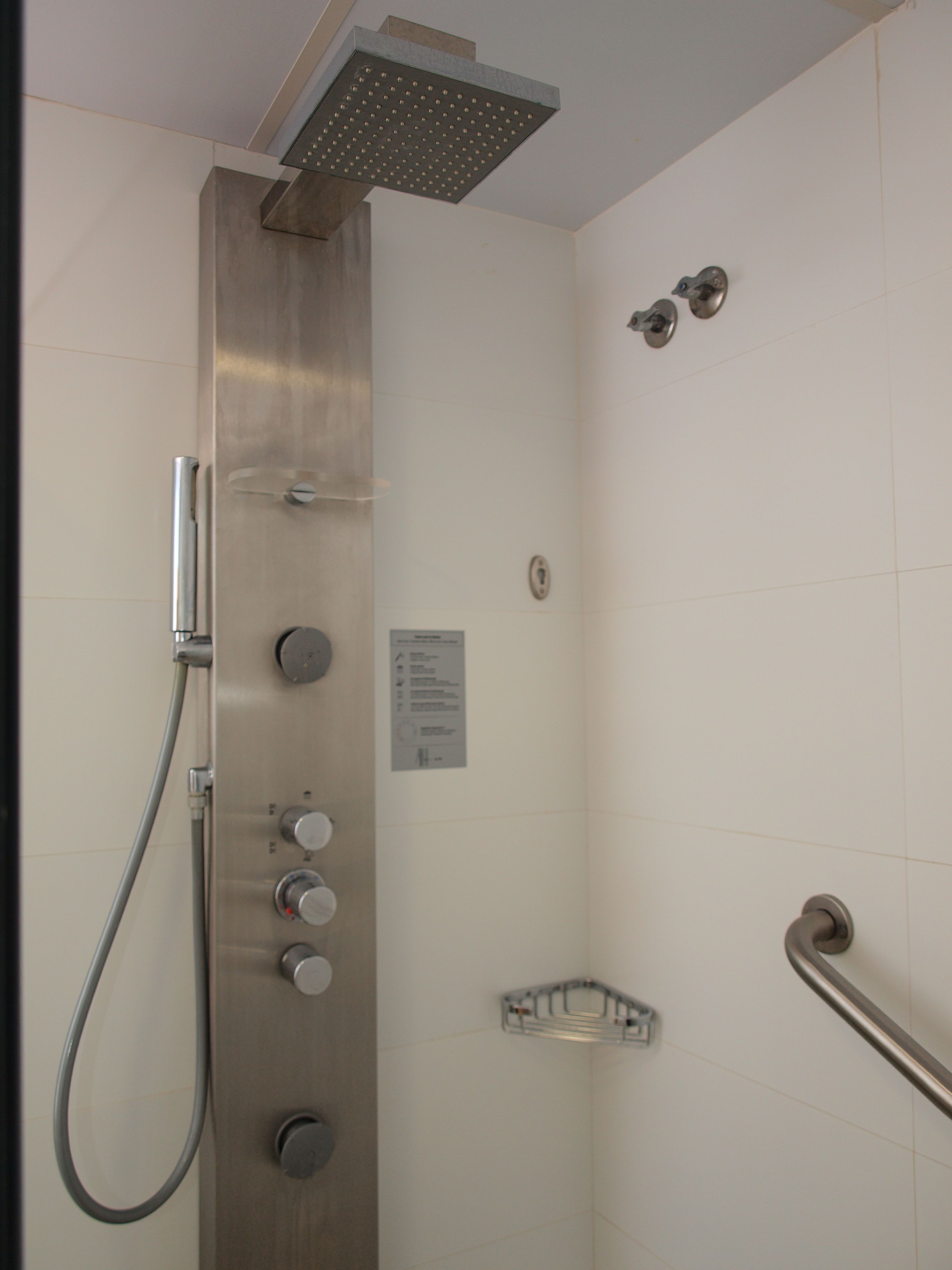 Ducha con cabezal de ducha de mano, panel de control en la pared y barra de apoyo.