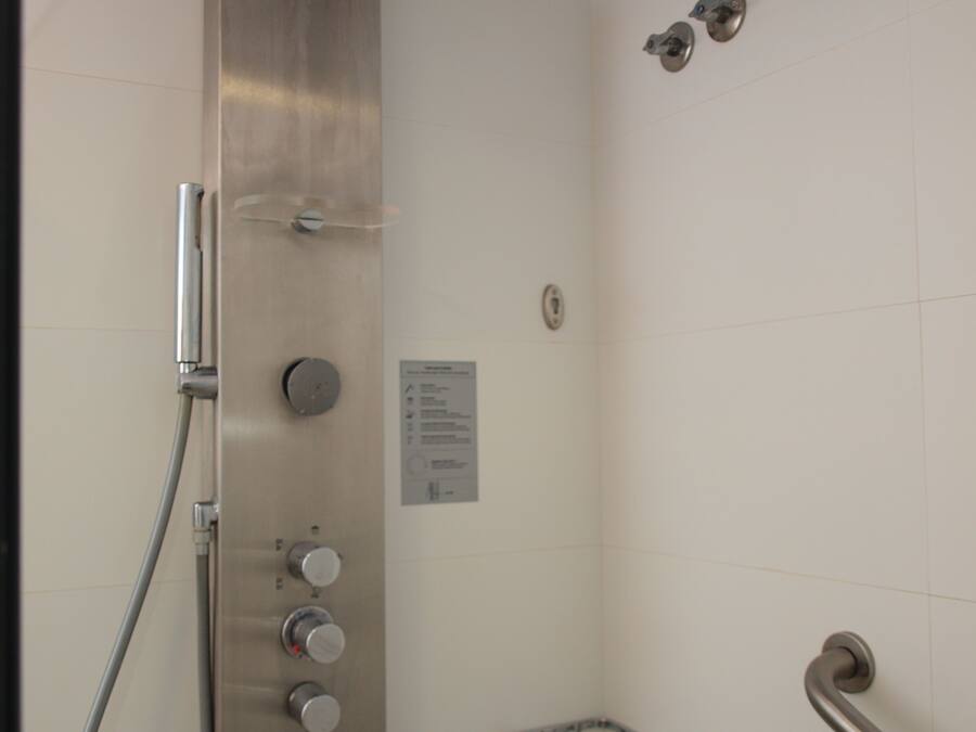 Ducha con cabezal de ducha de mano, panel de control en la pared y barra de apoyo.