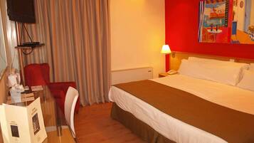Una habitación de hotel con una cama, un escritorio con silla, un televisor y un cuadro en la pared.