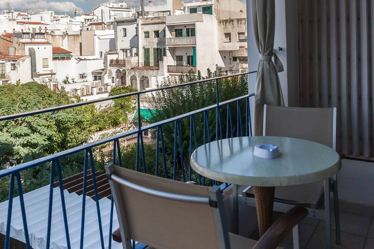 Ein Balkon mit Tisch und Stühlen mit Blick auf eine Stadtlandschaft aus Gebäuden und Grünflächen.