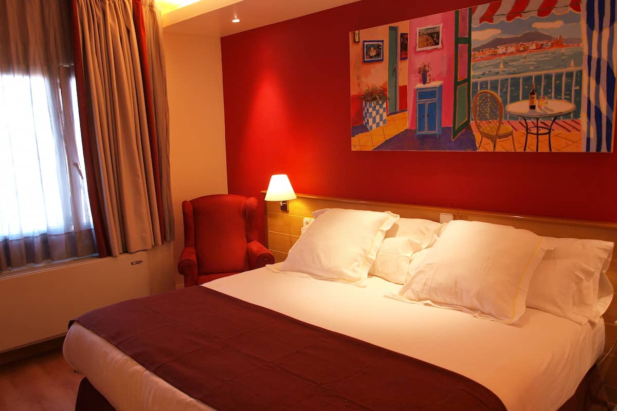 Ein Hotelzimmer mit einem großen Bett, einem roten Sessel, einem Tisch mit Lampe und einem Bild an der Wand.