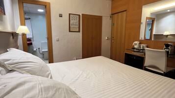 Habitación de hotel con una cama grande, un escritorio con silla, un espejo y una puerta que da a un baño.