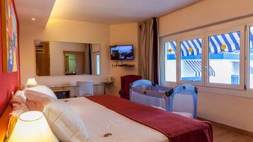 Habitación de hotel con cama, escritorio, televisor, silla, cuna y ventana con vista a un edificio.