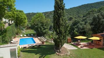 A swimming pool surrounded by lounge chairs, a barbecue area, and a view of a forested hillside.
