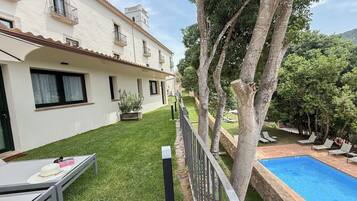 Zona junto a la piscina con vista despejada a una piscina, césped y un edificio con balcones.
