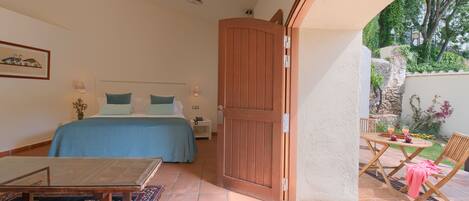 A bedroom with a bed, bedside table, and a view of the garden through an open door.