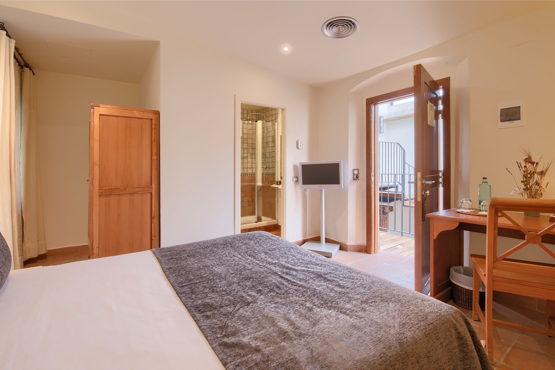 Habitación de hotel con cama, televisión, escritorio de madera y baño visible a través de una puerta abierta.