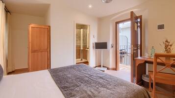 Habitación de hotel con cama, televisión, escritorio de madera y baño visible a través de una puerta abierta.