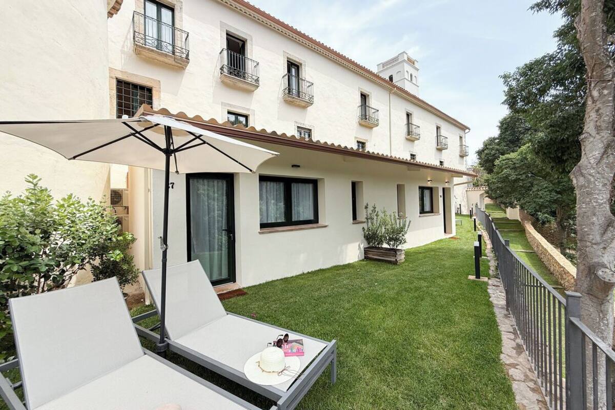 A courtyard with a white building, a small garden, and a seating area with a table and chairs.