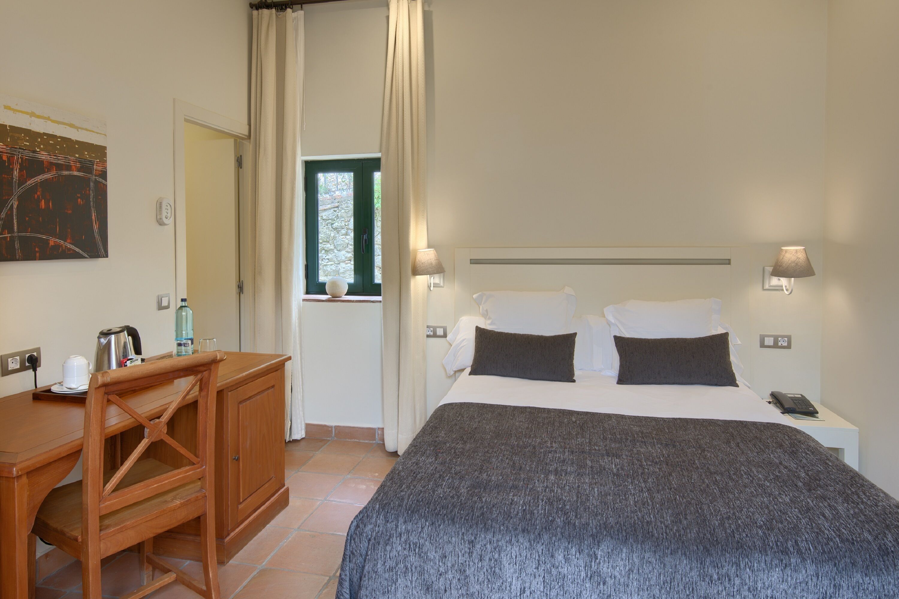 A bedroom with a bed, bedside lamps, a desk, and a window with curtains.