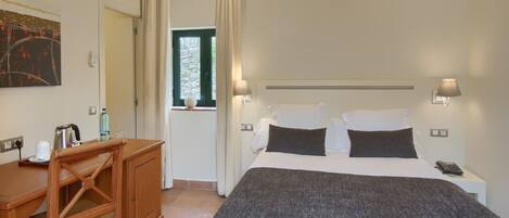 A bedroom with a bed, bedside lamps, a desk, and a window with curtains.
