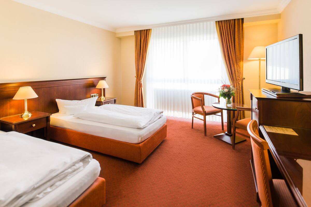 A hotel room with two beds, a desk, a chair, a television, and a window with curtains.