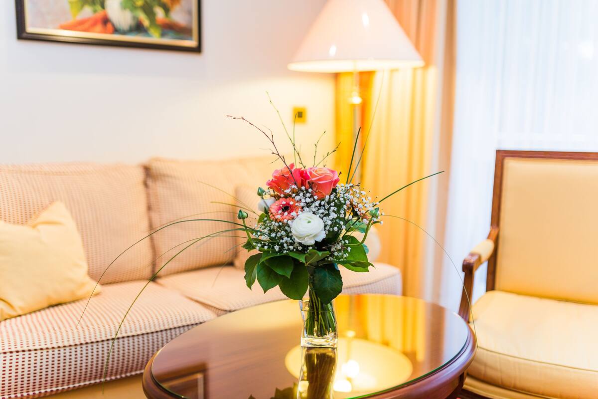 A living room with a sofa, a chair, a glass table with a vase of flowers, and a lamp.
