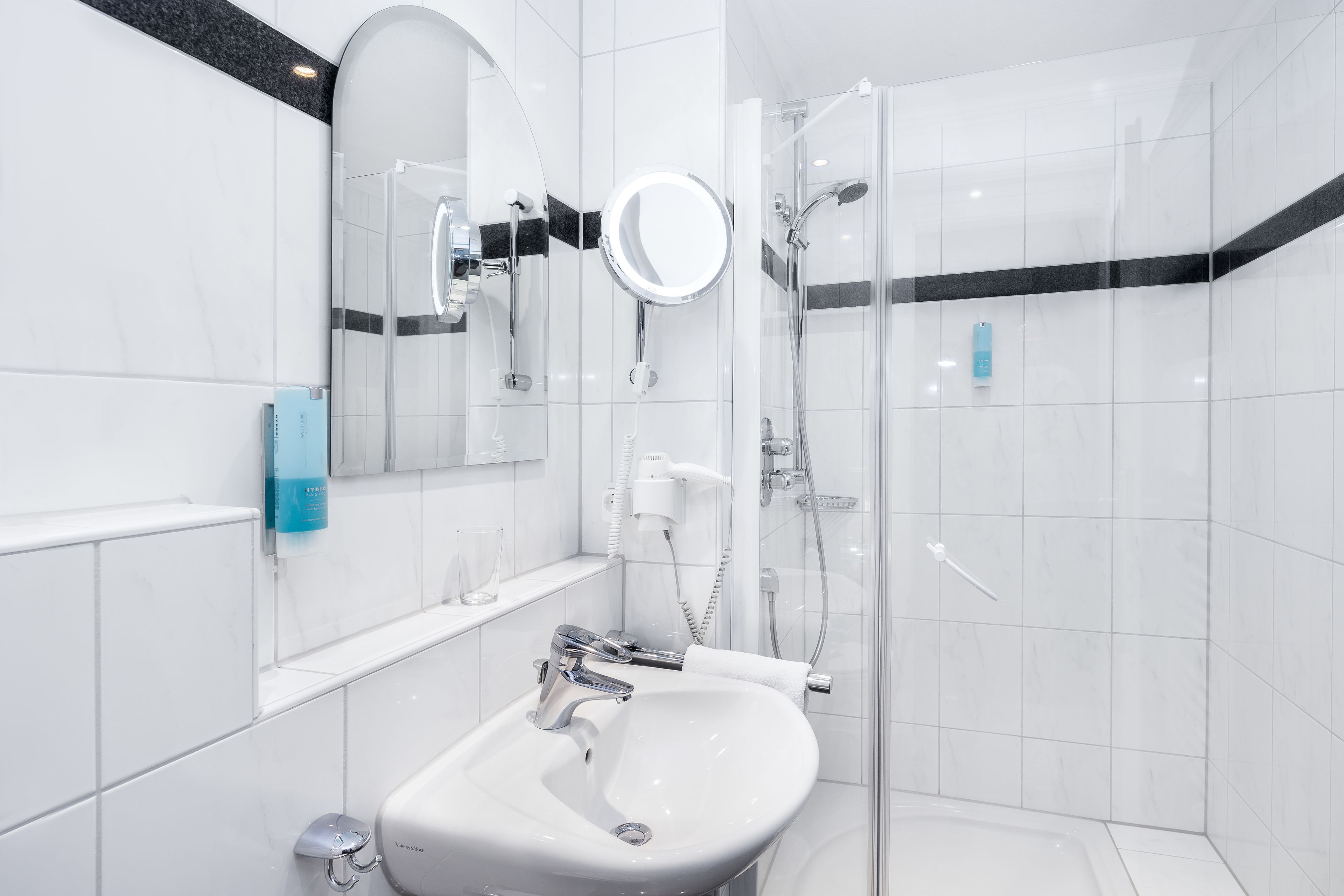 Ein modernes Badezimmer mit einem weißen Waschbecken, einem Spiegel und einer Duschkabine.