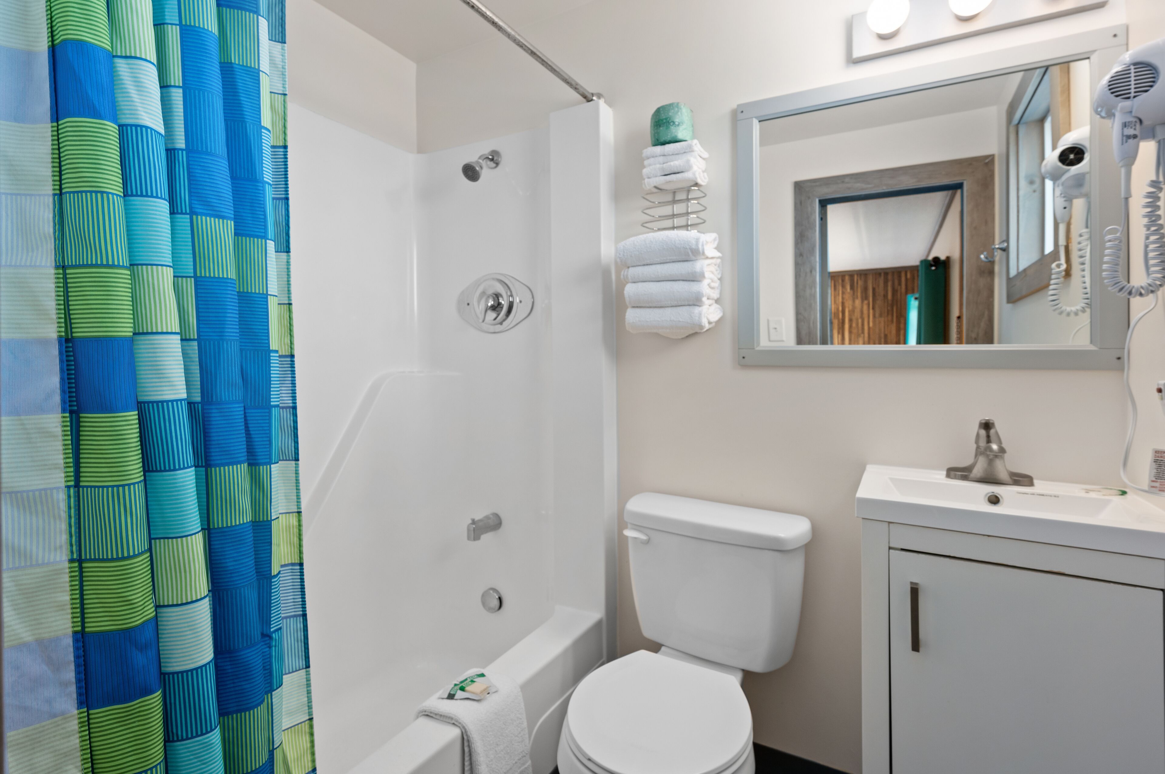 A bathroom with a shower, toilet, sink, and a mirror with a hairdryer.