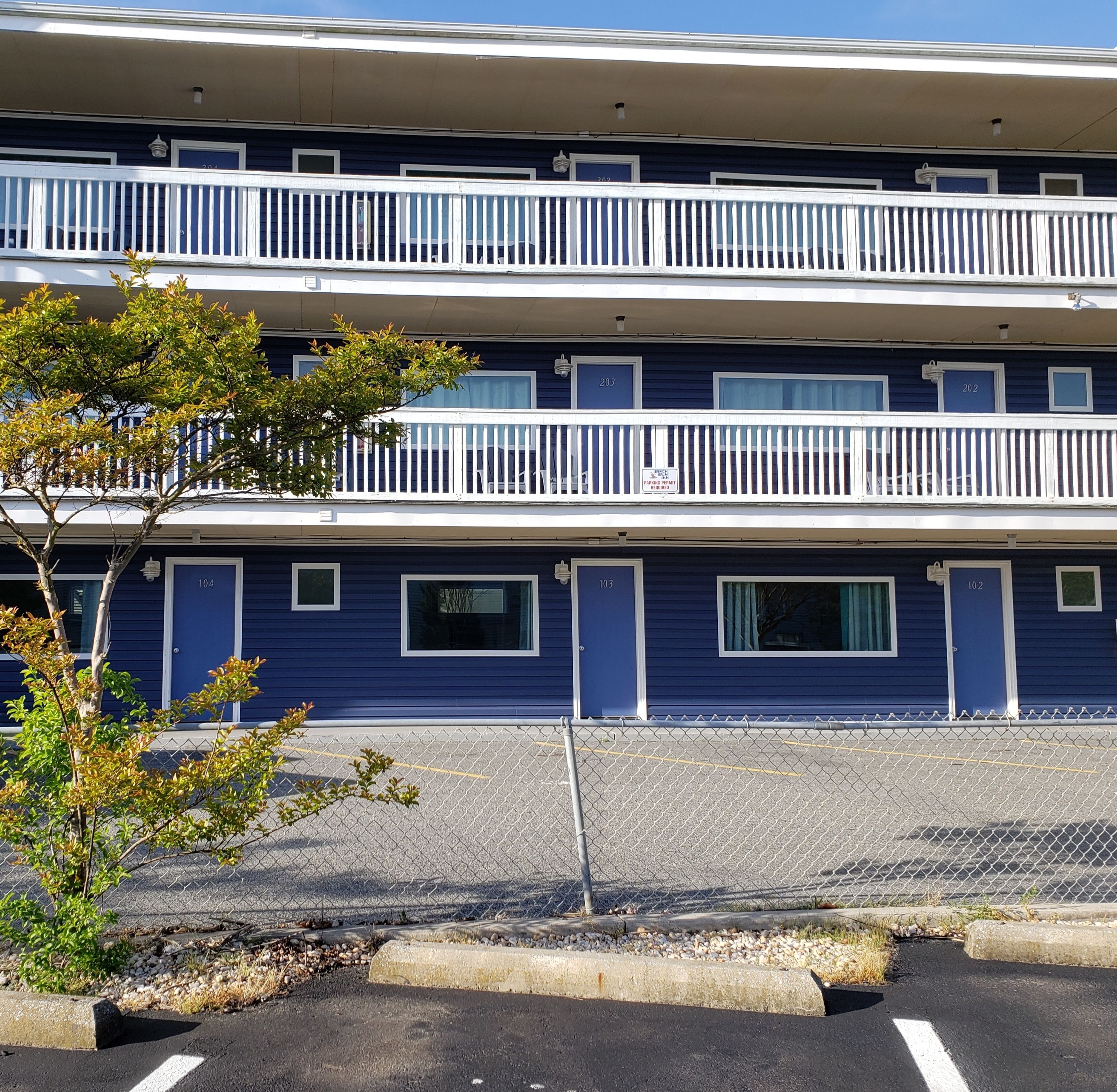 Un hotel de varios pisos con balcones, números de puerta y un estacionamiento.