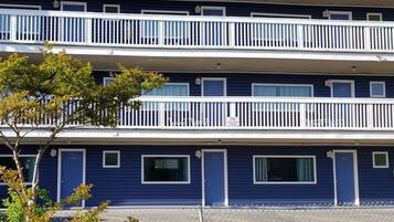 Un hotel de varios pisos con balcones, números de puerta y un estacionamiento.