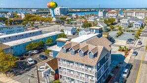 A multi-story hotel with a prominent balcony on the second floor, a parking lot in front, and a view of the waterfront in the background. - Beach Bum Inn (Ocean City)
