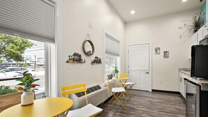 A modern kitchen with a refrigerator, a dining area with yellow chairs, and a large window with blinds. - Beach Bum Inn (Ocean City)