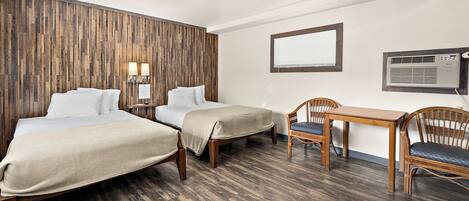 Quarto de hotel com duas camas, uma mesa pequena, uma cadeira, ar condicionado na parede e uma janela com persianas.