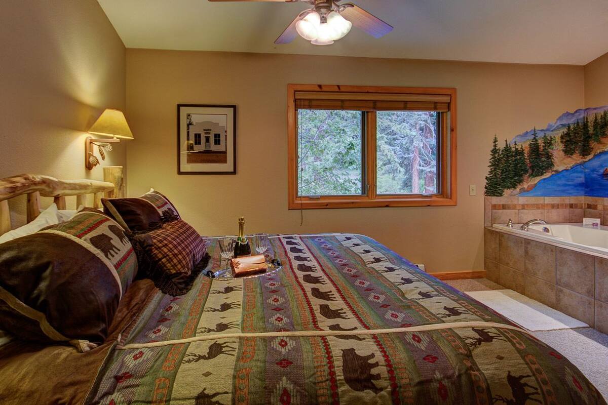 Un dormitorio con cama, mesita de noche, ventana, un cuadro y baño con bañera.
