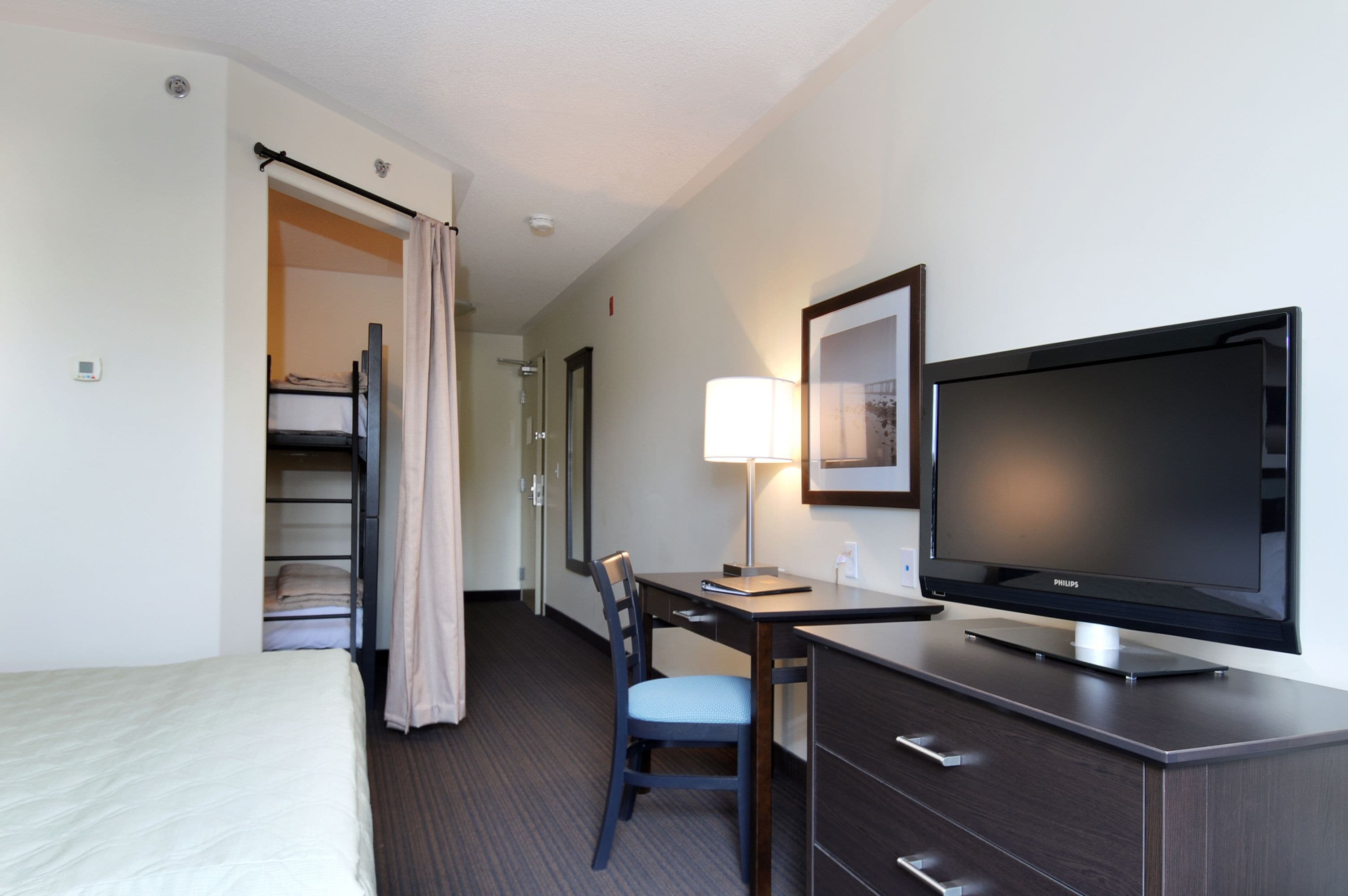 Une chambre d’hôtel comprenant un lit, un bureau avec une chaise, une télévision, une lampe et une armoire.