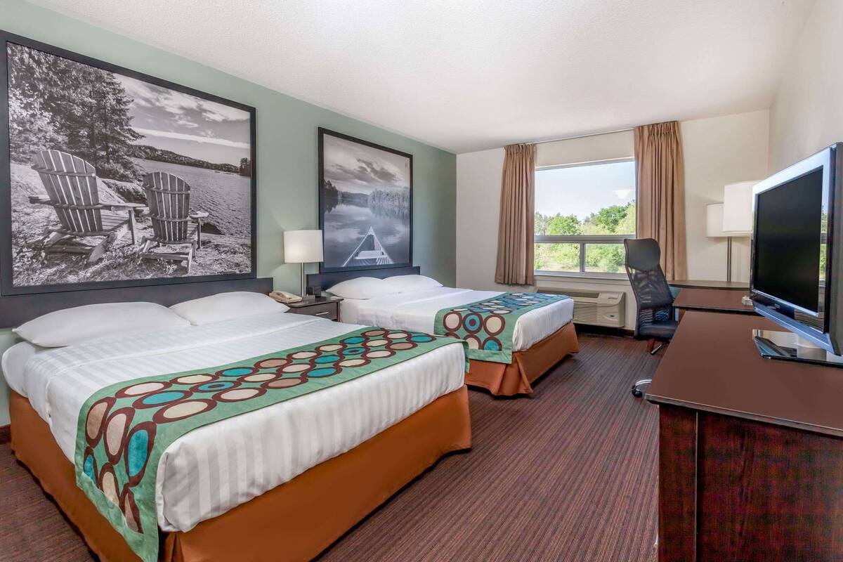 Una habitación de hotel con dos camas, un escritorio con televisor y ventanas grandes.