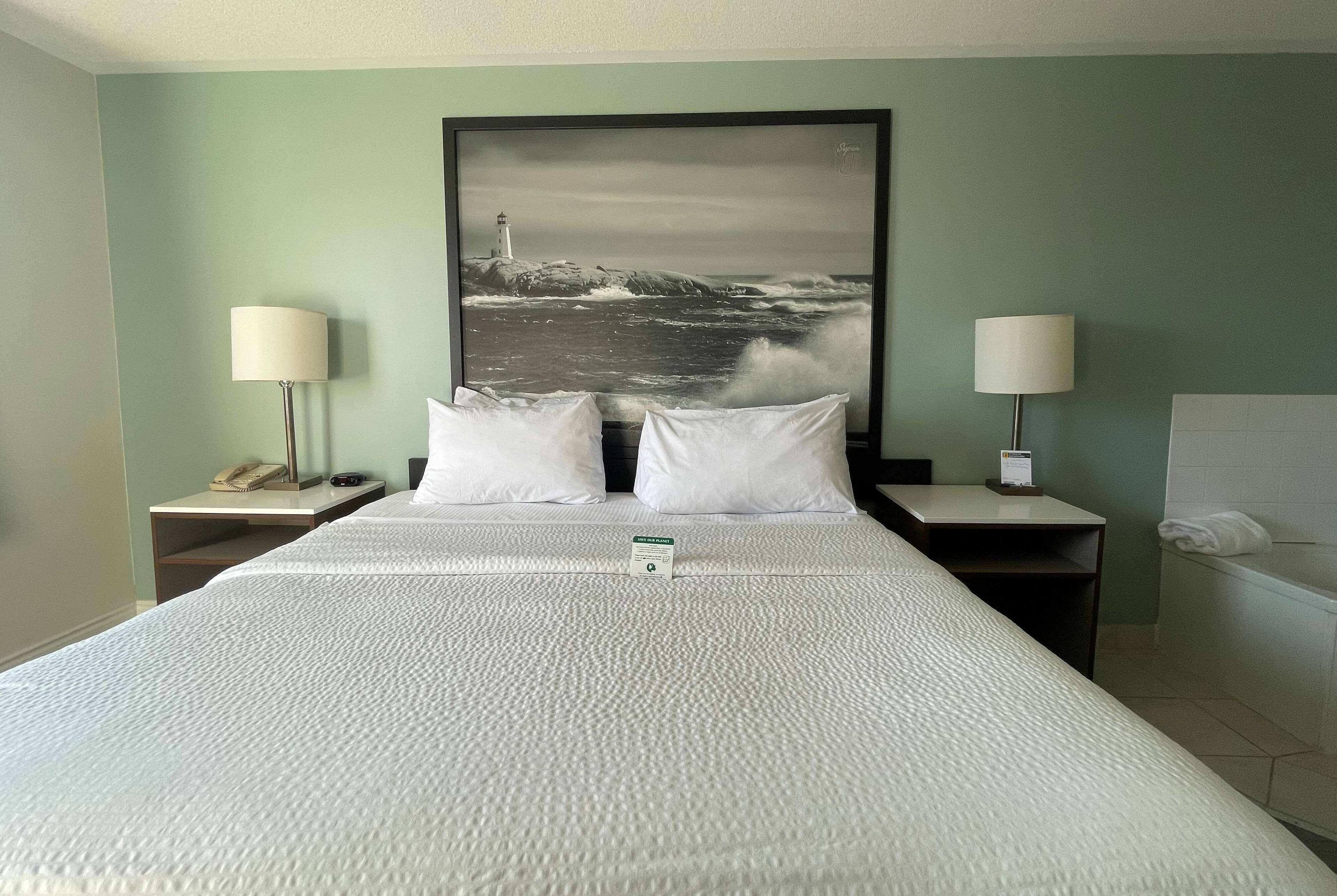 A hotel room with a large bed, two bedside tables with lamps, a nightstand with a phone, and a framed picture of a lighthouse on the wall.