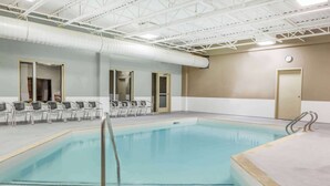 Una piscina interior con superficie de agua cristalina, rodeada de sillas y un suelo de baldosas.